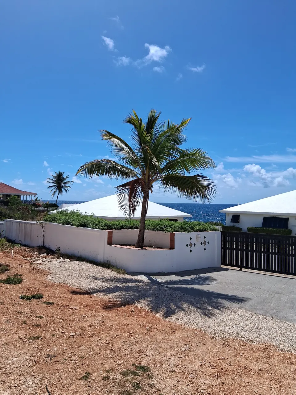 White coastal luxury property with dual hip roofs and coconut palms by turquoise water in West End, Anguilla